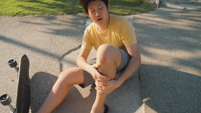 一名亚洲男孩在户外滑板运动中摔倒后膝盖擦伤。