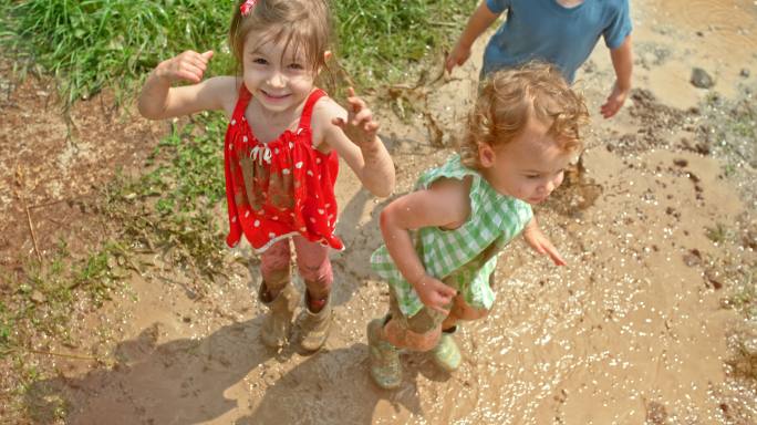 三个孩子在阳光下在泥泞的水坑里跳上跳下