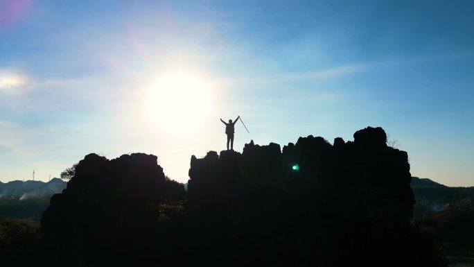 徒步旅行者登山成功-逆光站在山顶举手庆祝