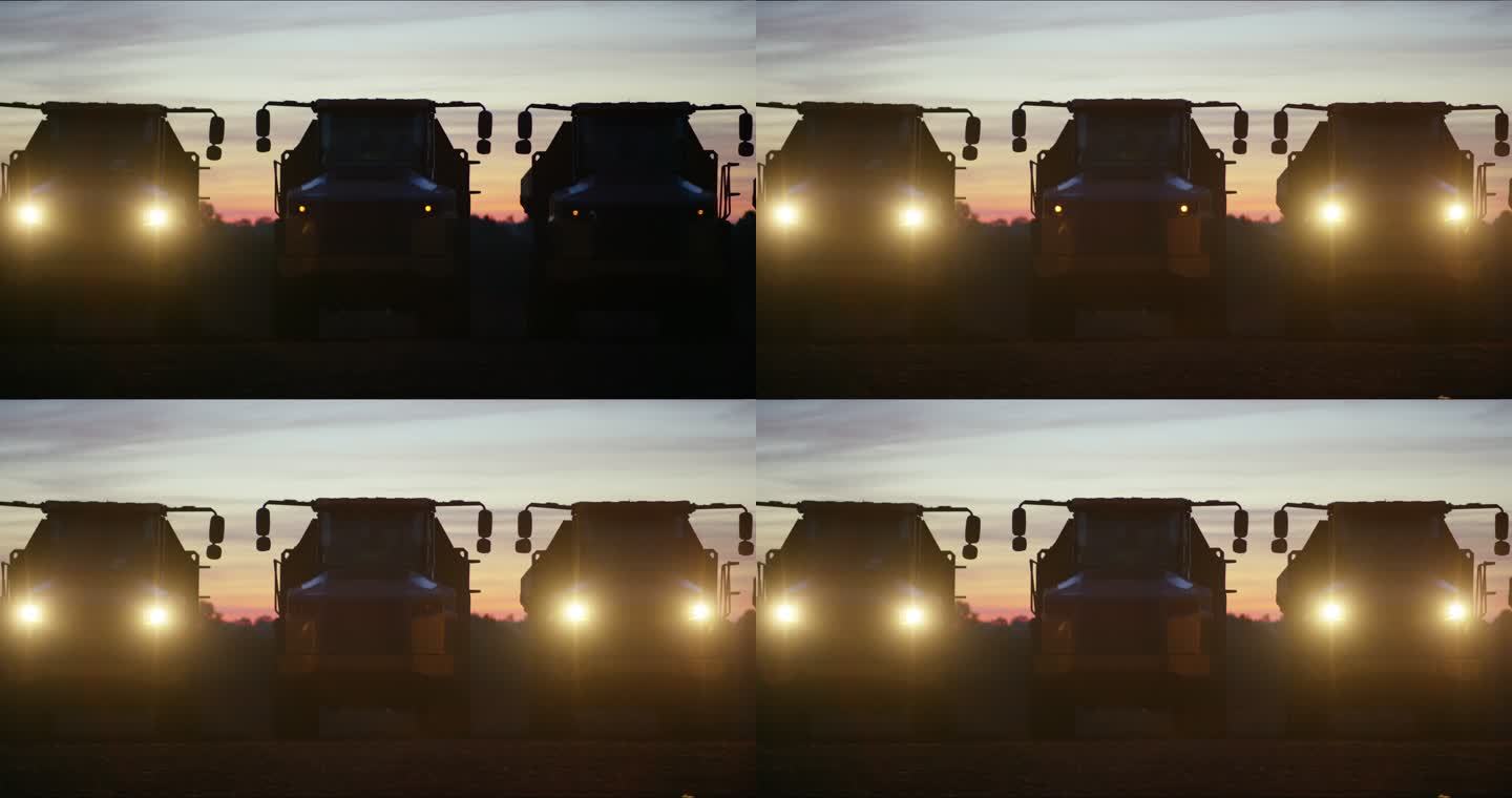 黄昏/黎明时分，三辆自卸车排成一行，前大灯闪烁