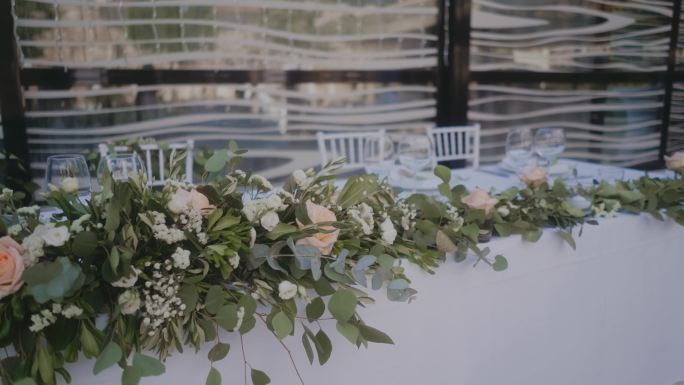 玫瑰和时尚的婚礼桌装饰。长长的除草桌，上面放着酒杯。