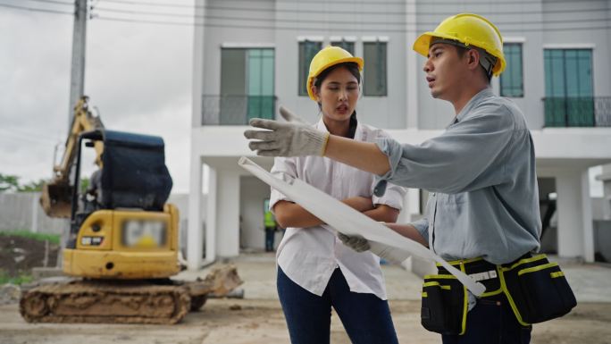 年轻的夫妇建筑师在住宅建筑工地讨论并查看蓝图。