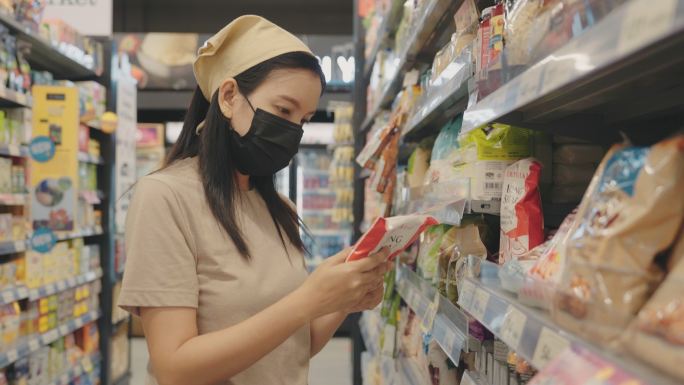 漂亮的年轻女子戴着医用口罩在超市里购买日常用品和杂货。家庭烹饪生活方式