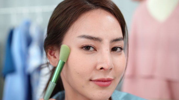 专注于美丽的亚洲美容博主正在为初学者录制化妆教程和美容小贴士，介绍如何将腮红从耳朵扫到颧骨，在脸颊上