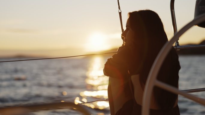 SLO MO女子坐在日落时航行的帆船甲板上