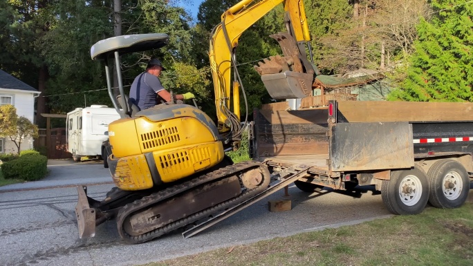 一名园林工人驾驶反铲车上了他的卡车