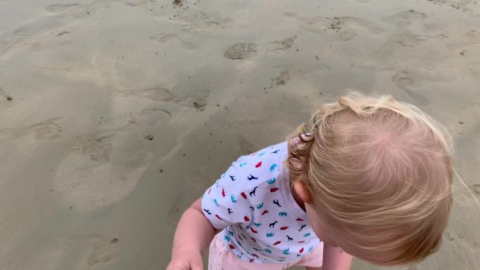 可爱的蹒跚学步的女孩在海滩上散步，靠近妈妈