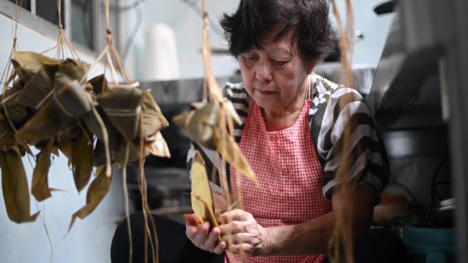 一位亚洲华裔资深女性在厨房里准备粽子饺子，放入配料并包装，为端午节做准备