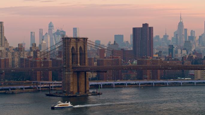 清晨黎明时分，从布鲁克林大桥下经过的渡轮上鸟瞰远景，背景是曼哈顿天际线的远景。无人机视频与摇摄相机运