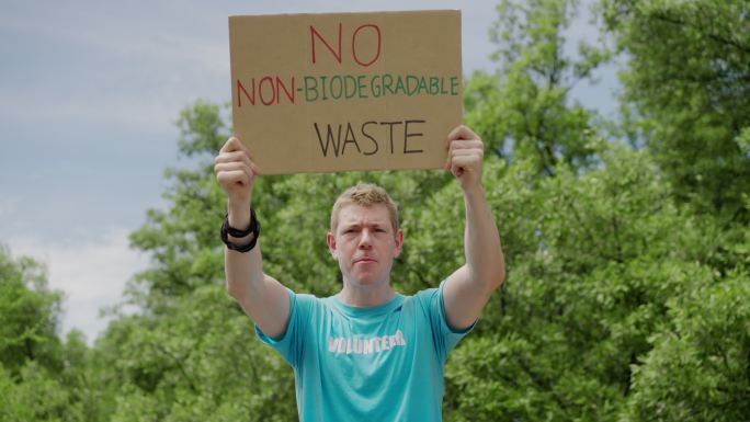 肖像，正面图：高加索年轻成年男子志愿者拿着纸板认真呼吁拯救地球，不要使用塑料，使用生物降解塑料，拯救