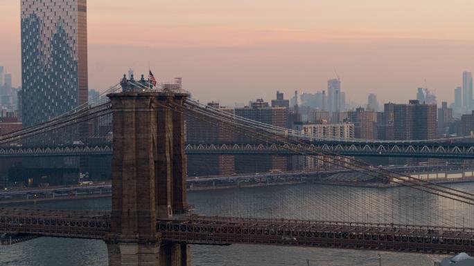 清晨黎明时分，近距离鸟瞰布鲁克林大桥塔顶的美国国旗，背景是曼哈顿天际线的远景。无人机视频与缓慢摇摄相