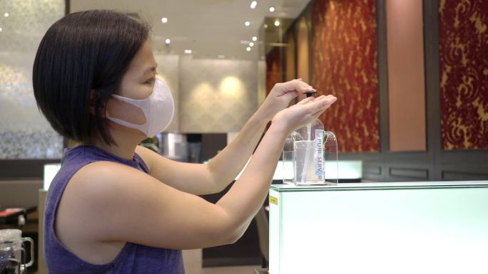 一名戴着防护口罩的亚洲女性在餐厅与家人一起吃了一些食物后，用酒精作为洗手液