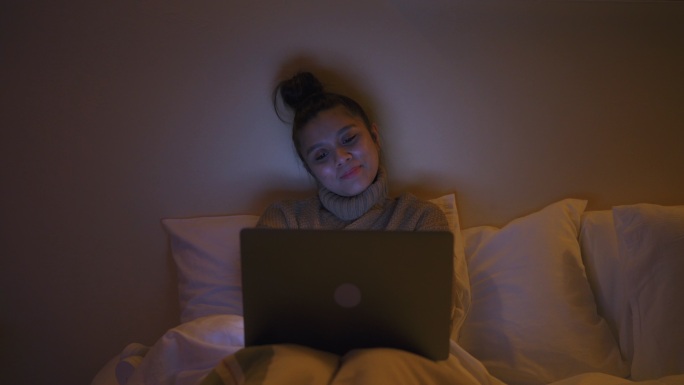 一位亚洲女性躺在床上用笔记本电脑看电影。