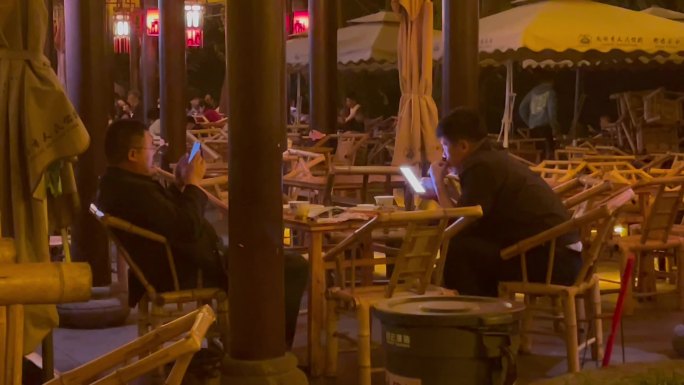 夜晚公园竹编椅喝盖碗茶刷手机的人们