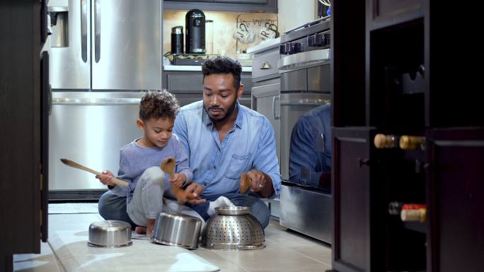 男孩和父亲在厨房地板上用锅当鼓