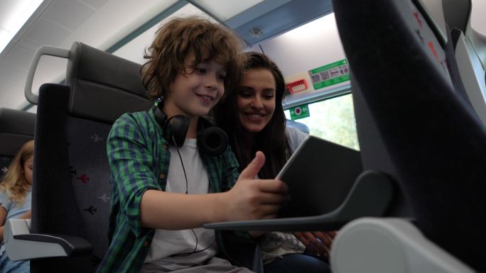 年轻的母亲在火车上通勤时，用平板电脑和儿子嬉笑怒骂