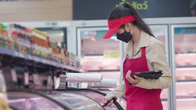 亚洲女超市员工用平板电脑检查冰箱里的新鲜食品