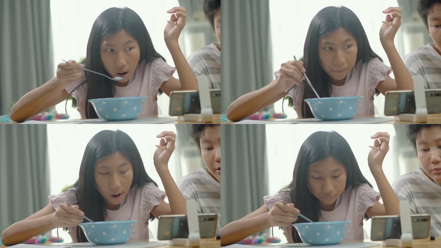 亚洲女孩和男孩在家里的餐厅里一起吃面汤，通过智能手机观看电影或病毒式视频，这是周末生活方式的概念。