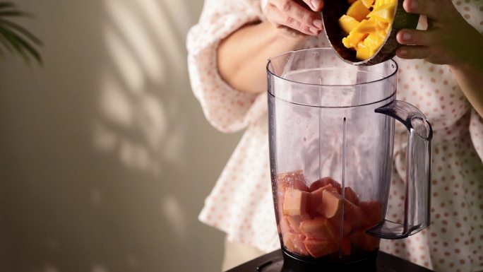 女人在搅拌机里用木瓜和芒果调制健康的冰沙