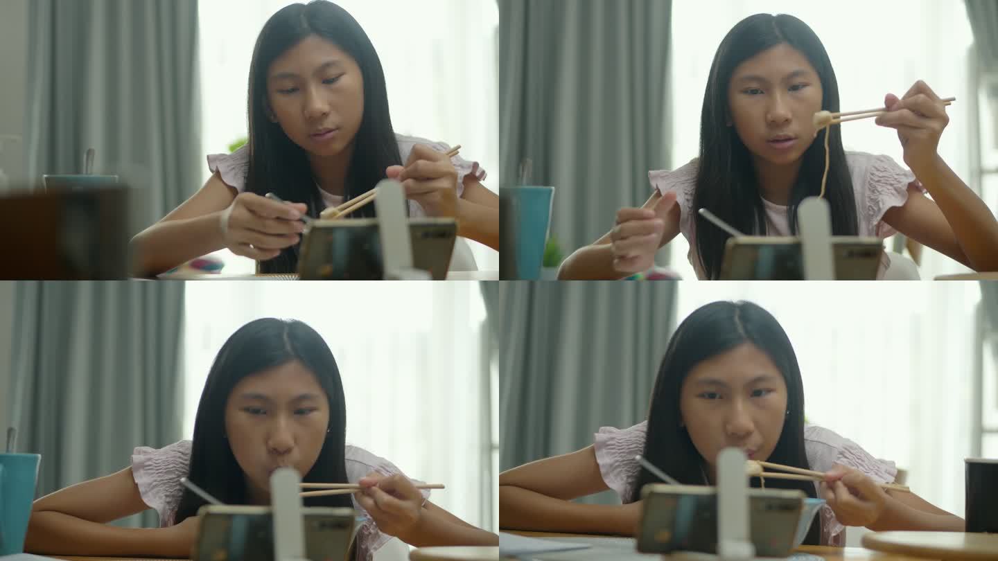 亚洲女孩在家里的餐厅里吃面汤，用智能手机看电影或病毒式视频，这是周末生活方式的概念。