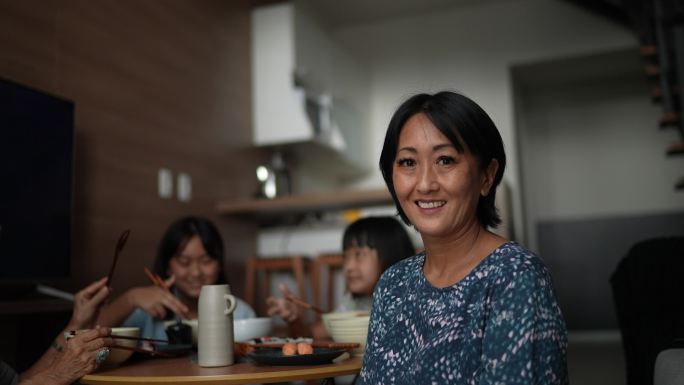 一位快乐的成熟女性在家与家人一起吃日本食物的肖像