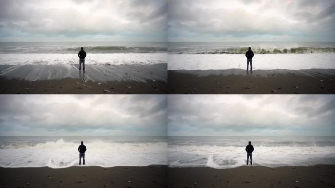 站在海滩上的男人。天空和巨浪笼罩。慢动作。