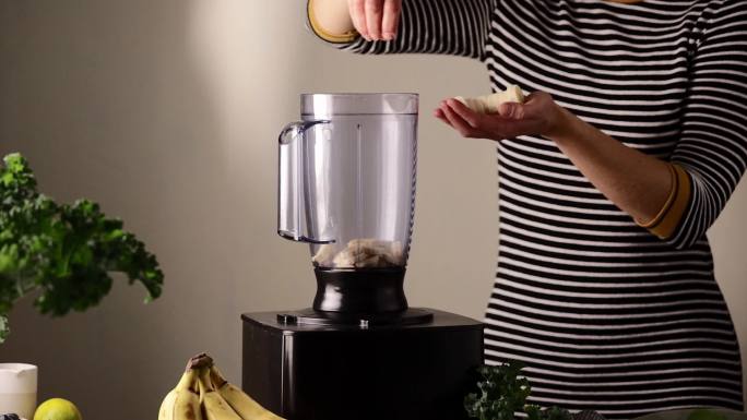 一名妇女在搅拌器罐中加入香蕉片的特写镜头