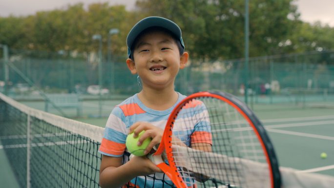 一个打网球的小男孩。一位可爱、微笑的男童网球运动员在球场上比赛后看起来很开心的肖像