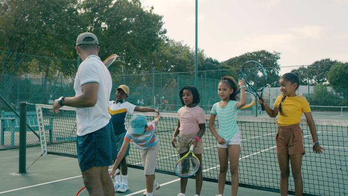 一群孩子和教练一起打网球。一个教快乐、可爱、多样的网球运动员在球场上使用球拍的人