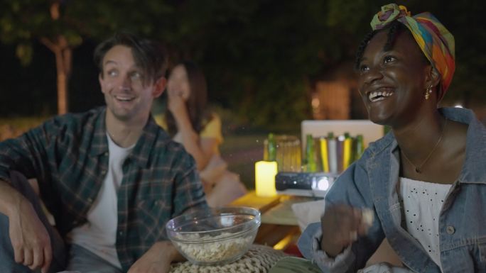 一群多种族朋友一边吃爆米花一边在投影屏幕上看电影