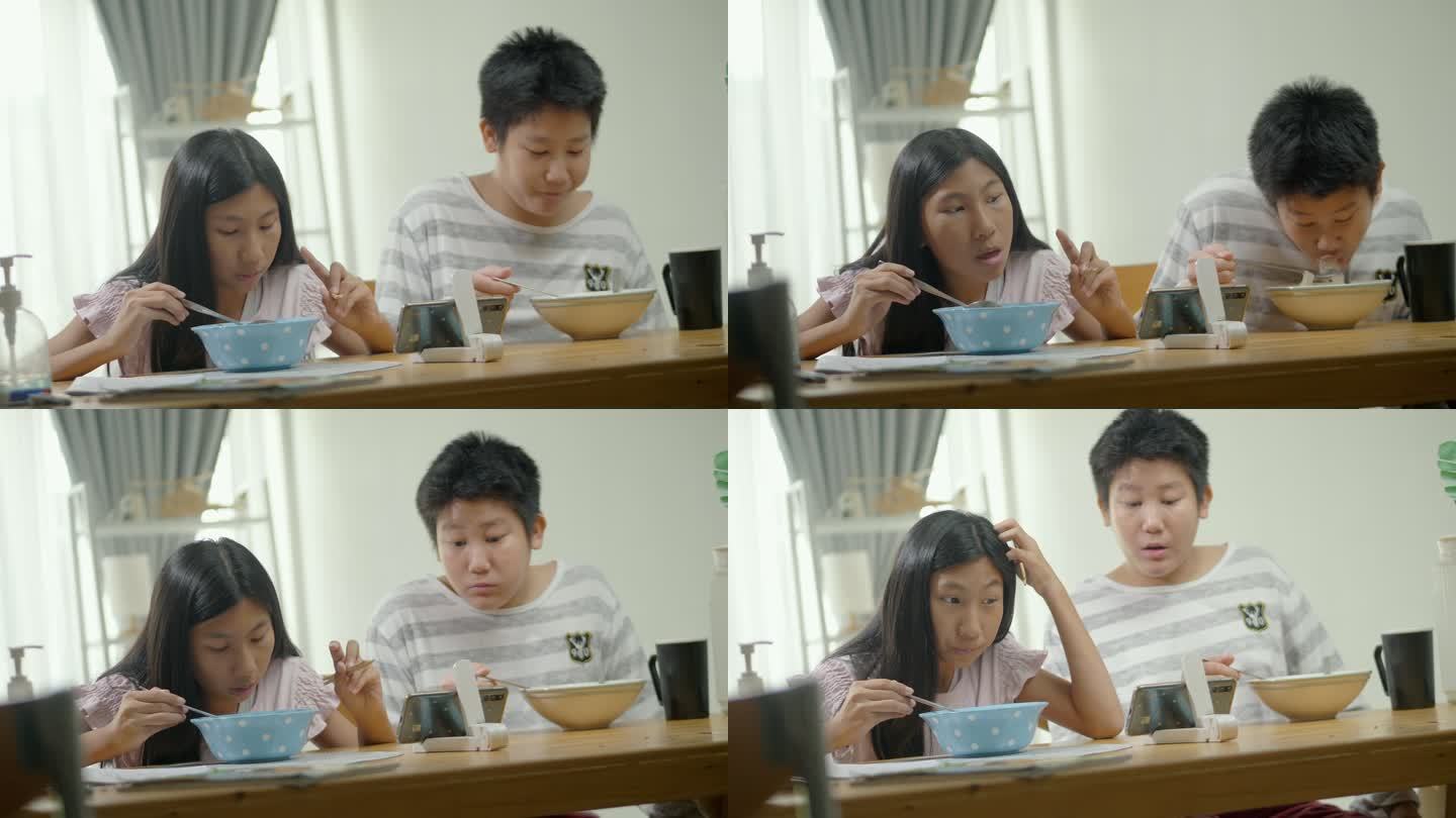 亚洲女孩和男孩在家里的餐厅里一起吃面汤，通过智能手机观看电影或病毒式视频，这是周末生活方式的概念。