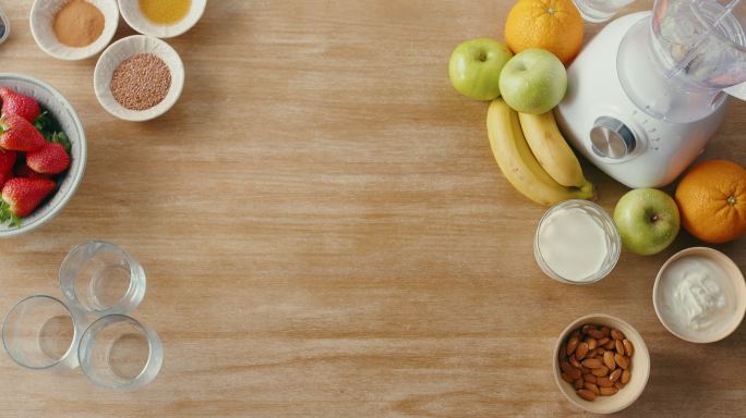 上图是新鲜水果和健康早餐冰沙搅拌机。草莓、蓝莓、覆盆子、苹果、坚果和酸奶放在一间空荡荡的厨房里。准备