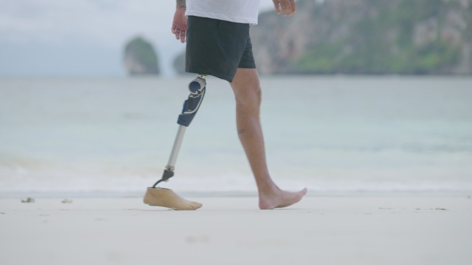 特写：一名戴假肢的残疾人早上在海滩上散步。残障收藏：日常生活理念。