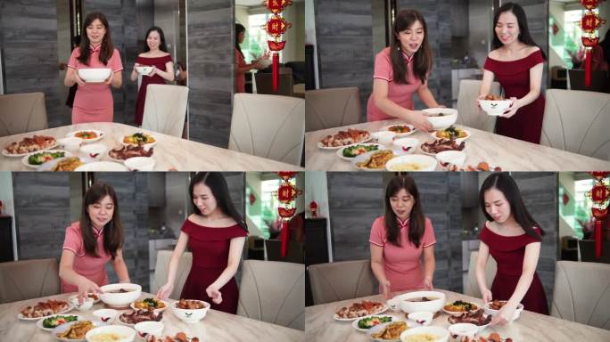 两个亚裔中国妹妹在中国新年期间从厨房里拿食物放在餐桌上