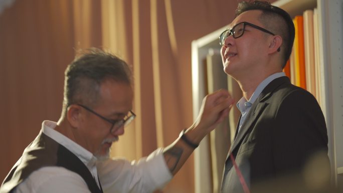 亚洲华裔高级男子裁缝用卷尺测量客户的体型，以便在工作室制作新西装，并用数字平板电脑记录下记录数字
