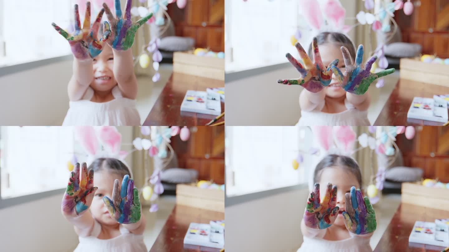 一个可爱的亚洲女孩戴着兔子头巾，用有趣的颜色给她的手着色。孩子们玩得很开心，准备复活节，画彩蛋和装饰
