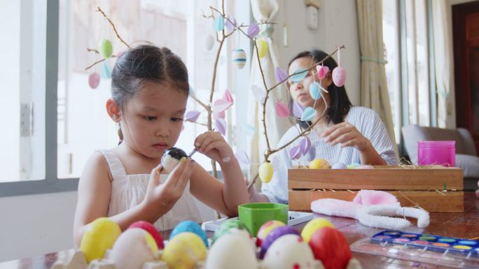 一个亚洲小女孩正和家人在鸡蛋上涂色。孩子和家人准备复活节，彩绘和装饰彩蛋。