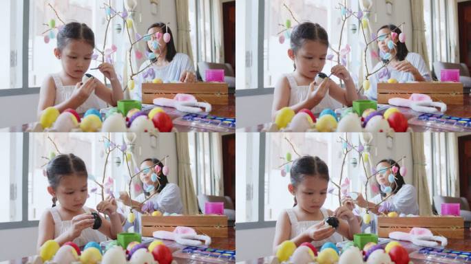一个亚洲小女孩正和家人在鸡蛋上涂色。孩子和家人准备复活节，彩绘和装饰彩蛋。