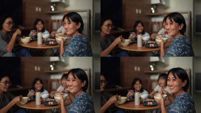 一位快乐的成熟女性在家与家人一起吃日本食物的肖像