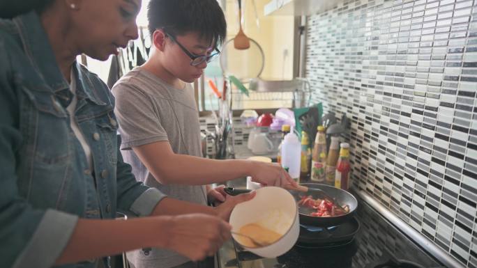 亚裔中国少年男孩在厨房做饭，他的养母在厨房