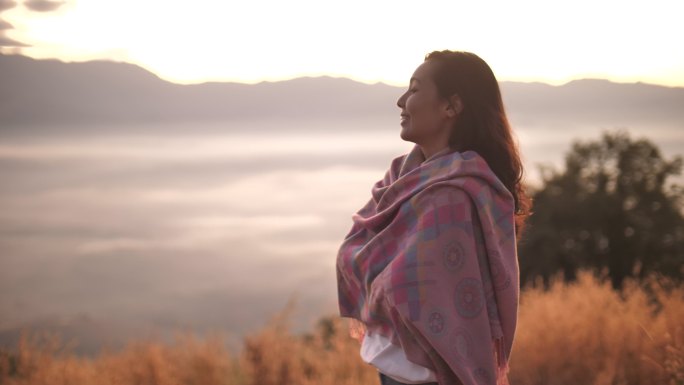 自由亚洲女性站在山顶，欣赏日落美景