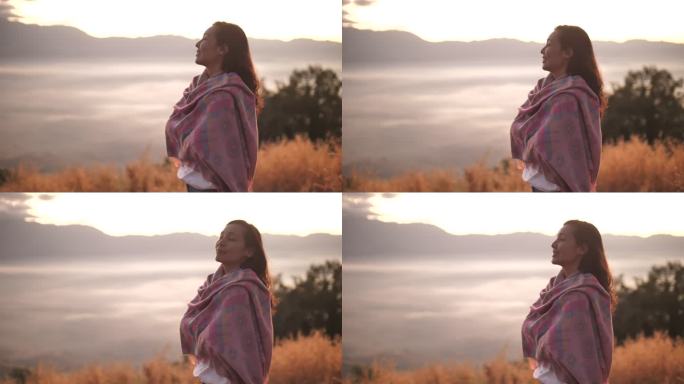自由亚洲女性站在山顶，欣赏日落美景
