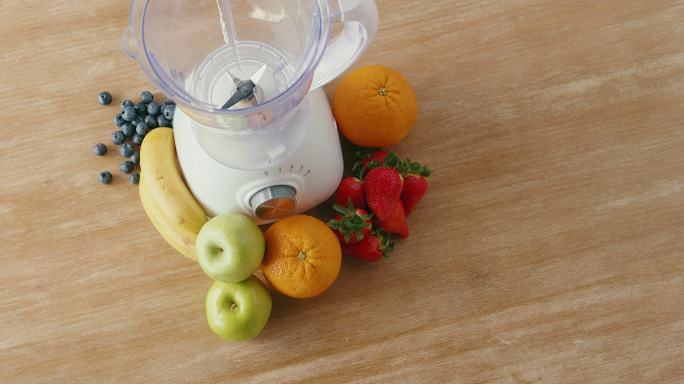 新鲜草莓、香蕉、青苹果、浆果和橙子的俯视图，以及用于制作健康奶昔的搅拌机。
