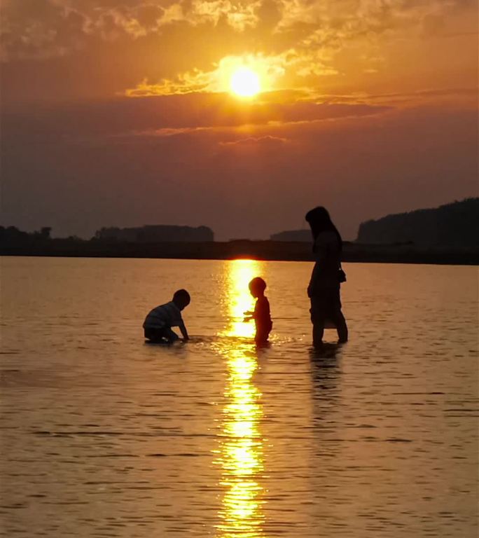 小河夕阳下两个小宝贝在妈妈面前玩水嬉戏竖