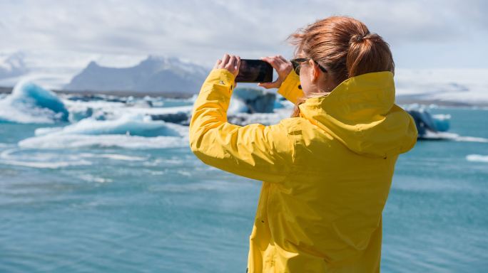 女游客用智能手机拍摄冰岛冰川泻湖和水鸟飞过冰面的照片