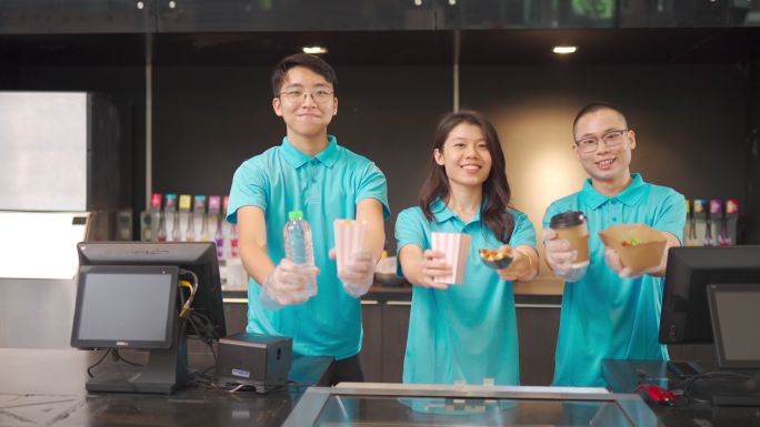 在电影院的特许摊位前，穿着制服的亚洲中式快餐工人微笑着看着镜头