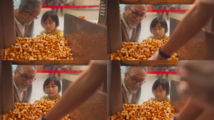 亚裔中国祖父孙女在娱乐大厦电影院电影院的特许权摊位上看着快餐店工人往纸桶里舀馅爆米花