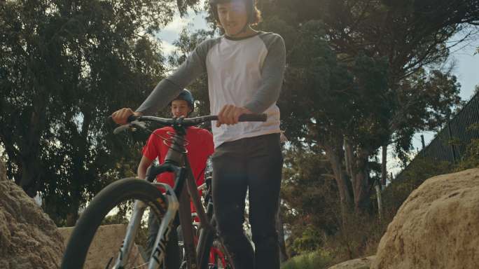 两名年轻的男性BMX自行车骑手，一边步行，一边将自行车推到泥土跑道上的坡道上，一边练习，为即将到来的