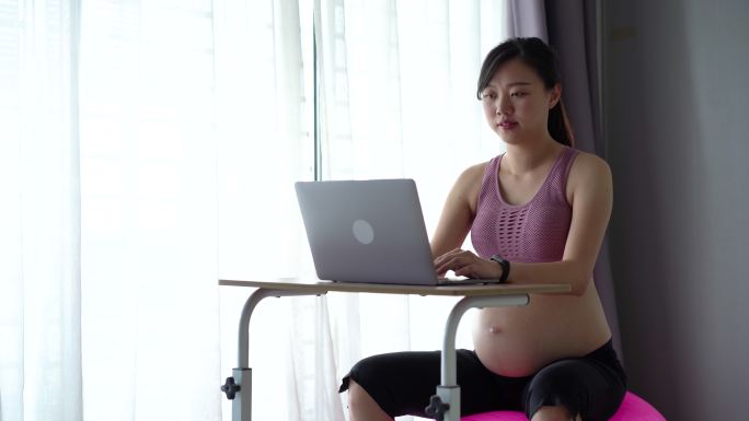 亚洲孕妇在家工作时坐在健身球上