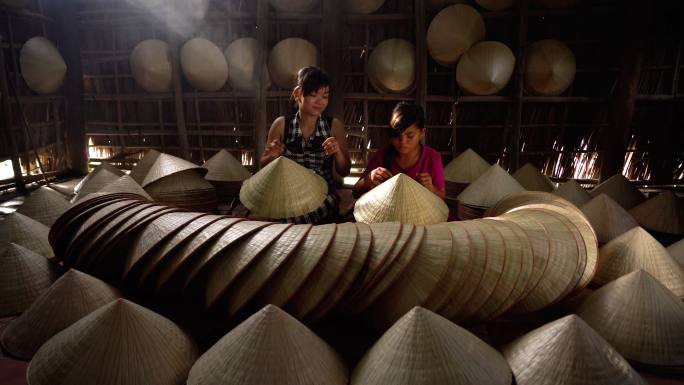 4k镜头越南工匠教女孩在越南坎特霍省阿普索菲村的老传统房子里制作传统越南帽的微光场景，传统艺术家概念